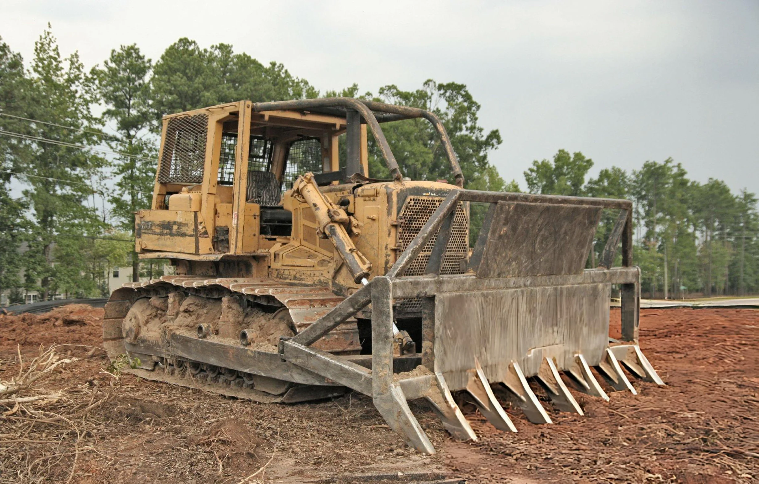 Bulldozer with a large rake attachment clearing dirt at a construction site