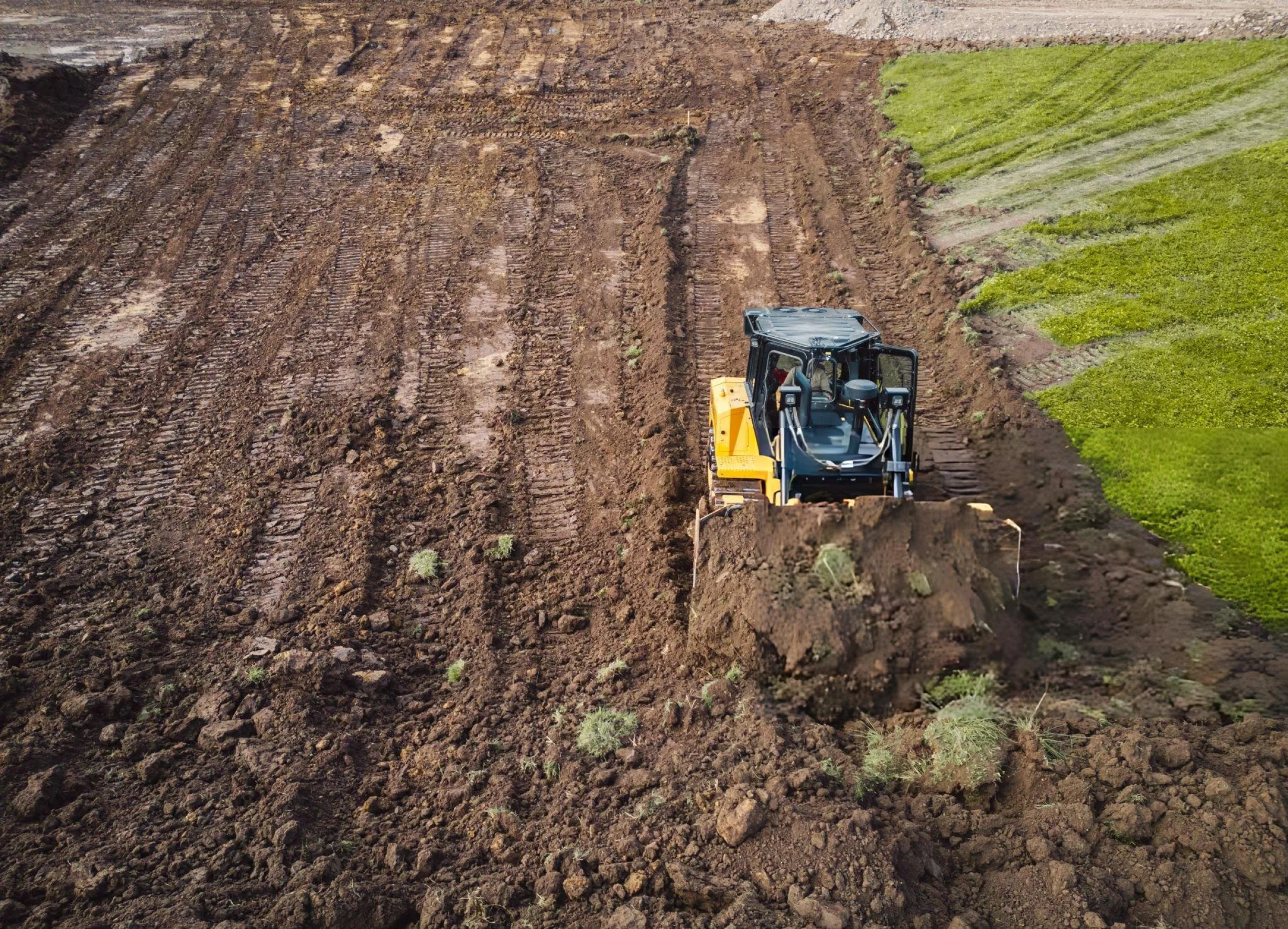 Skid steer loader moving soil across a large cleared construction site