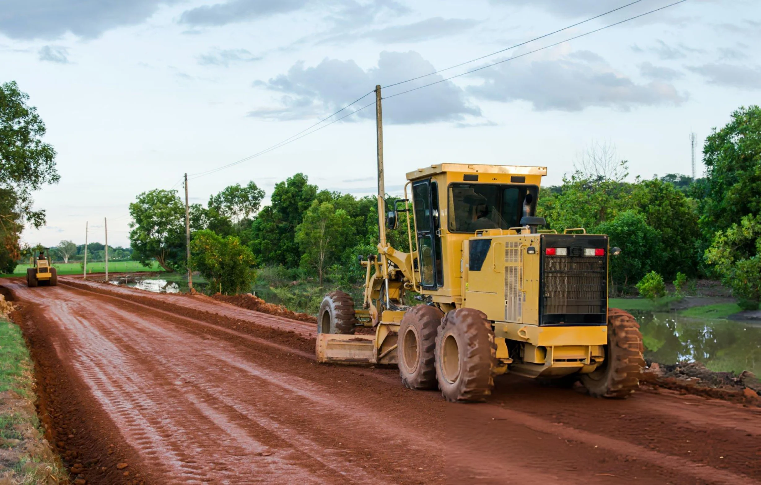 Yellow road grader levelling a dirt road in a rural area